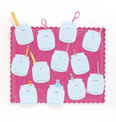 a pink and white place mat with calendars hanging on it's sides, along with pens and pencils