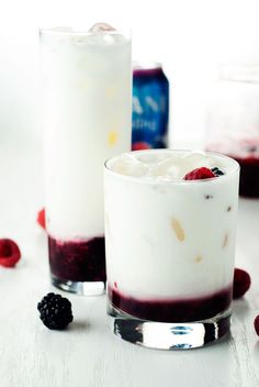 two glasses filled with ice cream and berries next to each other on a white table