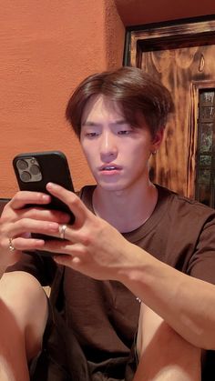 a young man sitting on the floor looking at his cell phone while holding it in his hand