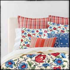 a white bed topped with lots of pillows next to a pillow case filled with colorful flowers