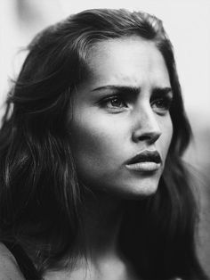 a black and white photo of a woman with her hair blowing in the wind, looking off to the side