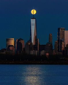 the moon is setting over the city skyline as seen from across the water in front of skyscrapers