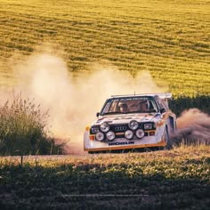 an old car driving down a dirt road in the middle of a wheat field with dust coming from its tires