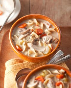 two bowls of chicken noodle soup on a wooden table