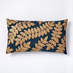 a blue and gold embroidered pillow with leaves on it, against a white wall background