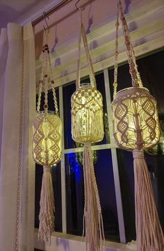 three hanging lanterns with tassels and lights on them in front of a window