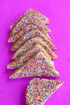 sprinkle covered cookies arranged in the shape of a christmas tree on a purple surface