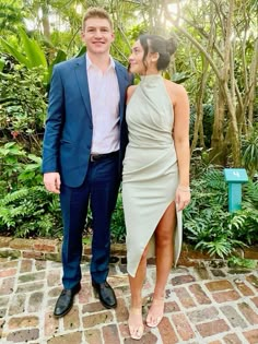 a man and woman standing next to each other in front of some trees with plants