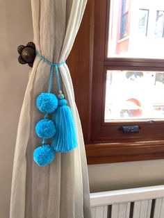 a curtain with blue pom poms hanging from it's side in front of a window