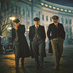 three men in suits and hats are walking down the street at night with their hands on their chins