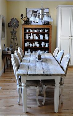 a dining room table with white chairs and an old fashioned china cabinet in the background