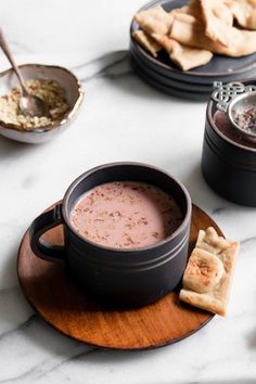 a bowl of soup on a plate with crackers and other foods in the background