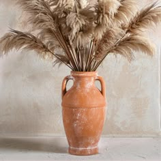 an orange vase filled with dry grass on top of a table