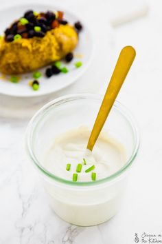 a glass bowl filled with yogurt and olives next to a plate of food