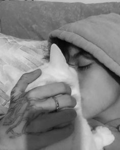 a woman laying on top of a couch holding a white cat in her hand and wearing a towel over her head