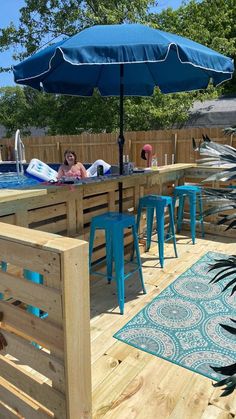 an outdoor bar with blue stools and umbrella in the middle of a wooden deck