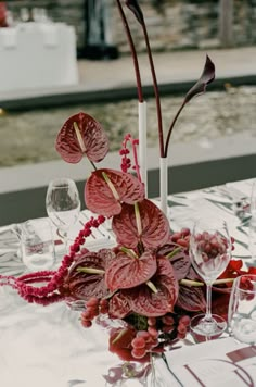 the table is set with red flowers and wine glasses