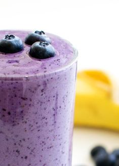 a blueberry smoothie in a glass next to bananas