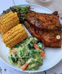 a white plate topped with meat and veggies next to corn on the cob