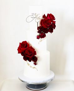 a three tiered white wedding cake with red roses on top