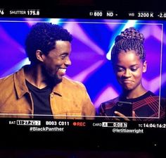 a man and woman standing in front of a tv screen looking at their cell phones