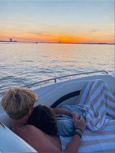 a man and child are laying in the back of a boat on the water at sunset