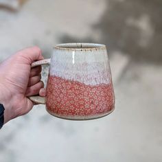 a hand holding a coffee mug with red and white speckles on the outside