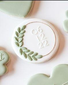 cookies decorated with green leaves and monograms are arranged on a white table top