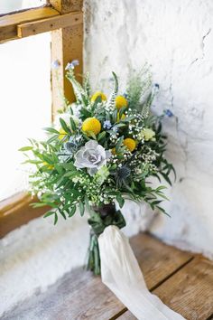 a bouquet of yellow and white flowers sitting on top of a wooden table next to a window