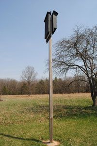 a street sign in the middle of a grassy field with trees and grass behind it