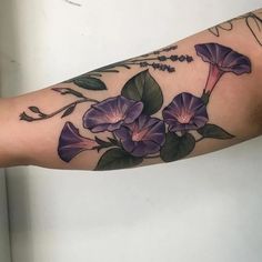 a woman's arm with purple flowers and green leaves on the inside of it