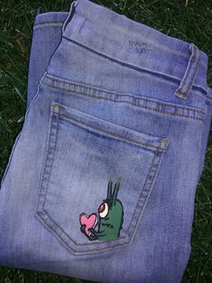 a pair of blue jeans with an image of a green frog sticking out of it's pocket