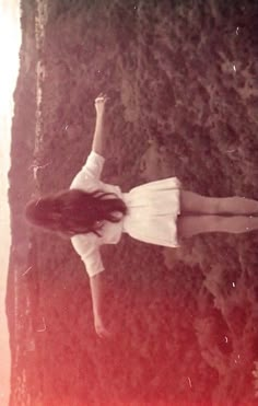 a woman in white shirt and skirt standing on grass with her hand up to the sky