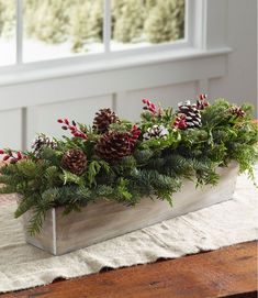 a planter filled with pine cones and greenery on top of a wooden table