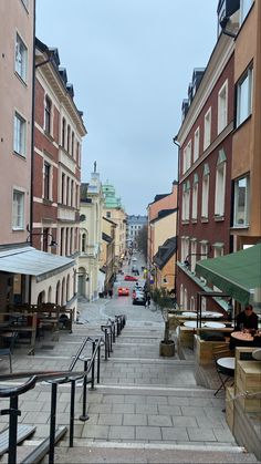 an empty city street lined with buildings and tables on either side of the road,