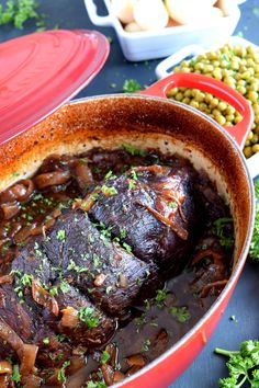 a red pot filled with meat and vegetables on top of a blue table next to green beans