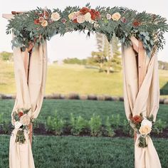 an arch decorated with flowers and greenery is set up in the middle of a field