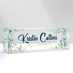 a clear plastic sign with blue flowers on it that says kriskin collins office manager