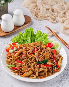 a white plate topped with noodles and veggies next to chopsticks on a table