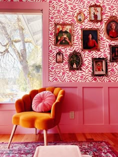 an orange chair sitting in front of a pink wall with pictures on it