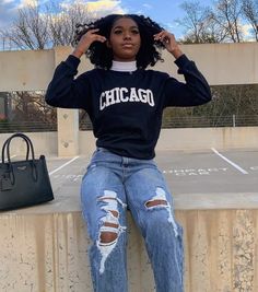 a woman sitting on top of a cement wall wearing ripped jeans and a chicago sweatshirt