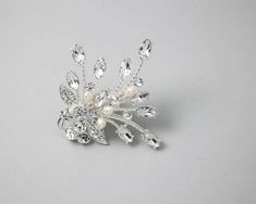 a brooch with pearls and crystal leaves on the front, sitting on a gray surface