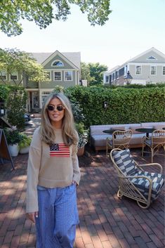 a woman standing in front of a house wearing sunglasses and an american flag sweater on