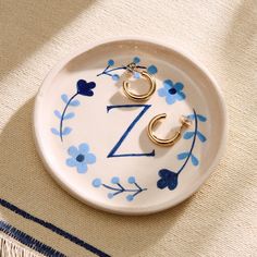 a white plate with blue flowers and two gold hoop earrings on the bottom that says z