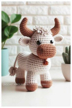 a small crocheted cow sitting on top of a table next to a potted plant