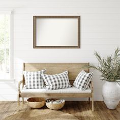 a living room with white walls and wood flooring is furnished with a wooden bench, two planters, and a large mirror hanging on the wall