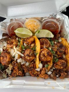 a takeout container filled with shrimp, onions and lime wedges next to drinks