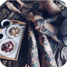 two people with tattoos on their arms and legs, one holding a plate of food