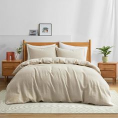 a bed with beige linens and pillows in a white room next to two wooden nightstands