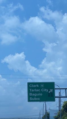 a green street sign on the side of a road under a blue sky with clouds